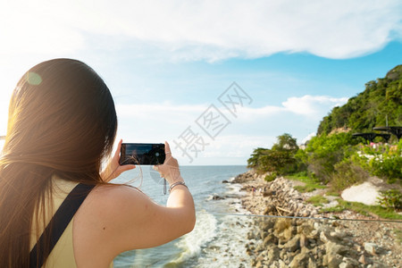 摩天大楼屏幕在智能手机上拍摄美丽海滩照片的女旅游客7月8日取景器图片