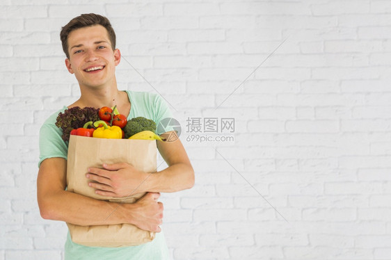 抓住携带买方着新鲜蔬菜水果杂货纸袋的笑着微青年男子图片