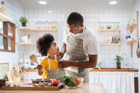 非洲快乐的父亲和儿子在白厨房烹饪前打扮在一起单身爸厨师与黑人小孩帮手穿黄色衬衣做饭在家眼接触关系聊天温暖家庭时看着彼此注i白色的图片