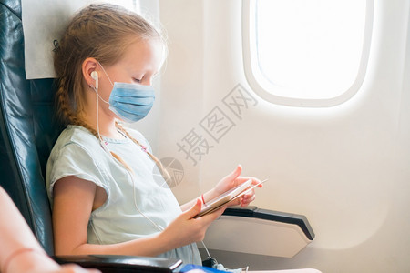 人们座位身戴外科面具的小女孩临保护由飞机进行保护防止Corona和牵着手的小姑娘乘飞机旅行可随身携带外科面罩的小女孩图片