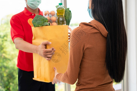 来自超市的亚洲送货员身戴面罩持有一袋新鲜食品蔬菜和水果供家里顾客使用特快杂货服务和新生活方式概念服务与新生活方式邮递员信使为了图片