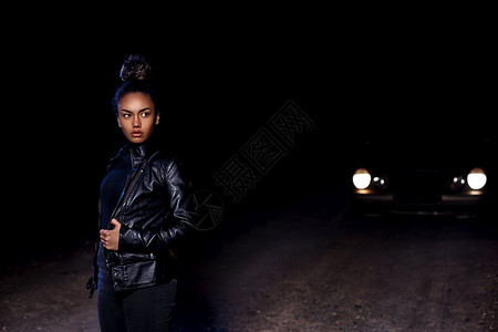 时尚身着皮夹克和黑衣服的非洲裔美国女孩穆拉托Mulatto在一辆废弃沙路上晚在车灯和光照亮下女士黑色的图片