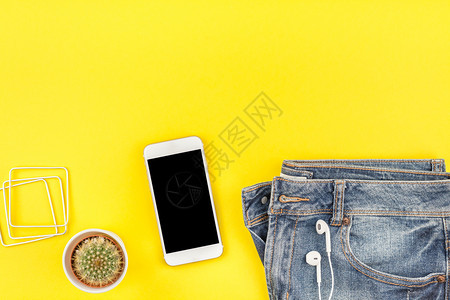 蓝色牛仔裤仙人掌和智能耳机的平板蓝色牛仔裤仙人掌和智能耳机印在粗黄色纸背景上并附有空间复制件春天手机时尚图片
