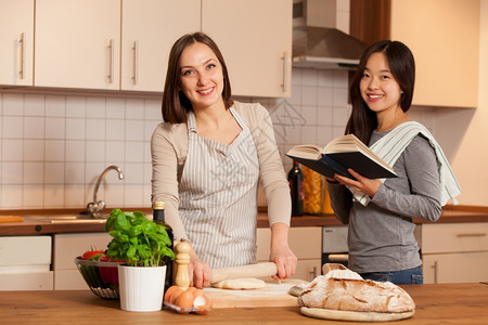 厨房协助滚动女人在赚钱而她朋友在看烹饪书时图片