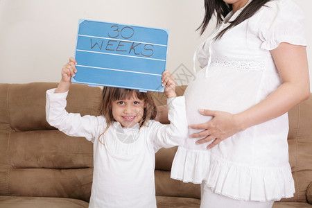 白种人卡斯蒂略女孩拿着30周的礼物给孕妇母亲签名成人图片