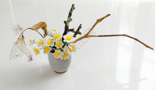 爱好用于家庭装饰的Daisy花瓶通过用白水泥面罩进行回收利用而使花盆变亮在白色背景上用黄活塞和干枯树枝编织小白花展示装饰风格图片