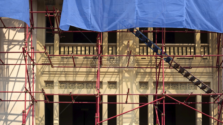 地点在翻修项目期间在建筑工地区古老的黄旧楼外面用梯子和蓝色网格板架挂红脚和蓝网板安全管道图片