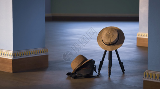 阴凉处关注挂在摄像三脚架上的女士帽挂在黑色照相袋上的Fedora帽子用古老音调风格的木地板上以蓝柱为基底的色子双头饰旅行概念目的图片