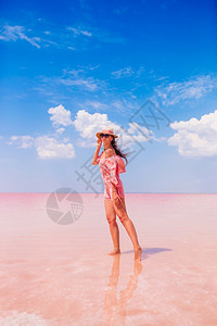 一种反射户外在阳光明媚的暑假日快乐女子在粉红盐湖上欢快的女子在阳光晴朗的暑假日戴着帽子的女人在粉红盐湖上行走图片