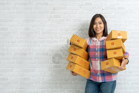 航运亚洲妇女携带棕色包裹或纸板盒在砖墙背景上服务人们图片