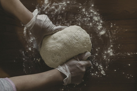 保持木制的在土耳其妇女用塑料手套在桌子上做面团的手意大利图片