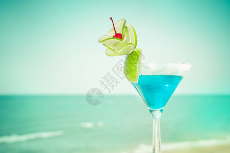 酒馆假期俱乐部蓝色玛格丽塔鸡尾酒在热带海洋滩的滨上配有石灰水果和樱桃装饰品的蓝色玛格丽塔鸡尾酒图片