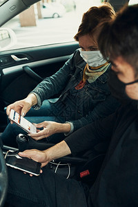 爆发关心坐在车里的男女用智能手机戴面罩避免感染防止疾在出现冠状腺毒时蔓延b使用智能手机戴上面罩以防止感染疾传播保护的图片
