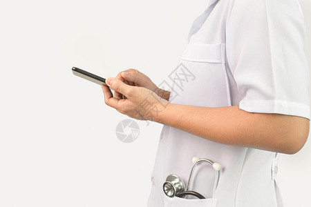 站立自信的年轻女医生使用智能手机口袋里装有听诊器站在白色背景之上护士专业的图片