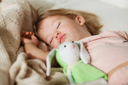 睡着的小女孩无忧虑的睡梦小宝床上有一个柔软玩具的小婴儿近身肖像一个美丽的睡童在编织的毯子上枕头一种房间图片