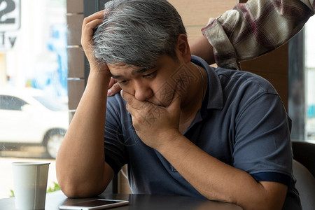 玻璃沟通40岁压力和疲劳的中年亚洲男子正坐在快餐厅里有朋友站在后面鼓励帮助和的概念20世纪8年代到9悲伤图片