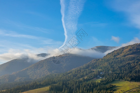 森尼山清晨和浅雾森林山区和异常云中的山坡上一个不寻常的云和几座房屋以及山坡上的早雾和异常云天堂树木繁茂图片