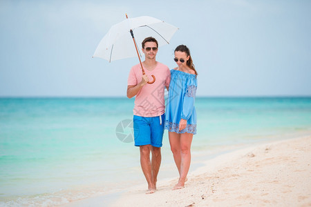 在海滩上快乐的年轻家庭带着雨伞躲避阳光白沙滩上两对的年轻家庭玩得很开心田园诗般的旅行蜜月图片