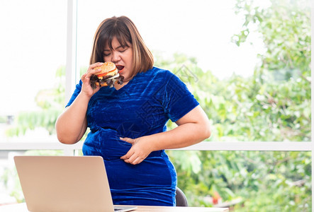 年轻的三明治饥饿超重妇女持有汉堡包在家工作期间体重增问题狂吃饮食紊乱概念BED食物图片