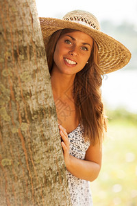 在公园的一棵树后面戴帽子的caucosian笑容女人的照片美丽成草图片