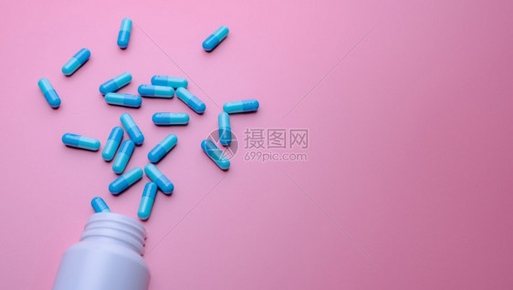 白塑料药瓶在粉红背景用旗条上散布的蓝色胶囊药丸分布在粉红底上的白塑料药瓶网店止痛品和抗生素物概念蓝色的颜粉彩图片