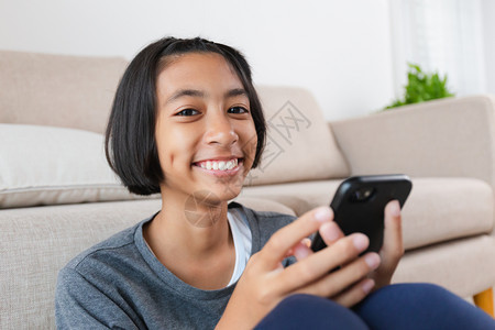 数字的小女孩使用智能手机观看在家中沙发上娱乐的视频这家小姑娘用智能手机观看影音在沙发上玩耍移动的社会图片