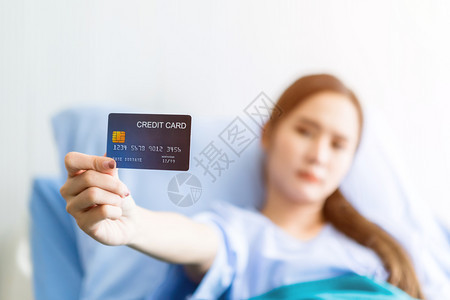 保持抽象的亚洲年轻女病人摘要与焦点模糊不清显示在房间医院背景支付疗治概念的床上持有一张信用卡并注明了费用输液图片