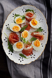 意大利沙拉煮鸡蛋烟熏火腿和白板上的花朵黑木本底芝麻菜胚芽午餐图片