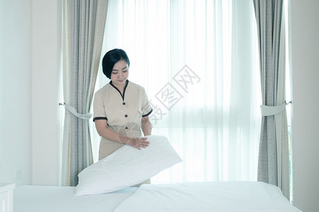 美丽的年轻亚洲美女佣在旅馆房间的床上铺枕头汽车旅馆泰国图片