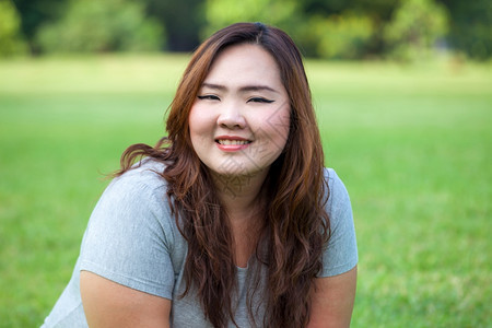 一种快乐肥胖的亚洲女人在公园外露面肖像日落图片