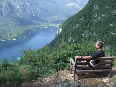 孤单的独男子坐在长椅上欣赏山地景观坐在里躺着的家伙Guy看着山和湖边的风景旅行者在山里休息斯洛文尼亚阿尔卑斯山脉观光旅游家孤独的图片