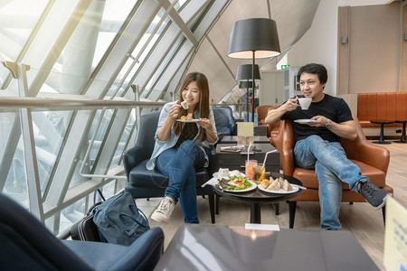 技术晚餐厅亚洲夫妇在现代国际机场等待航班旅行和运输概念时坐并吃着小客店机场休息室的亚洲夫妇座席和吃饭图片