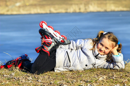 穿溜冰鞋的年轻女孩躺在地上微笑着年轻女孩穿滑溜冰鞋躺在地上滑轮松弛活动图片