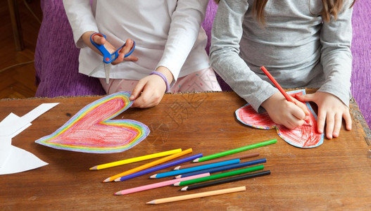 小女孩正在为母亲日或父情人节生画红和多彩的心胸年轻铅笔诺维科夫图片