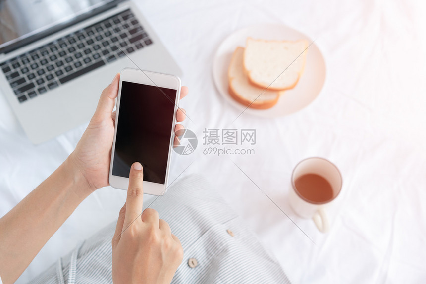 亚洲人黑色的手握和触摸黑智能手机屏幕的工作妇女手亚裔在吃面包咖啡和笔记本电脑时坐在白布上的亚洲妇女忙碌图片