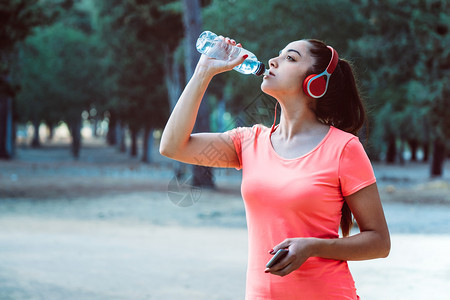 运动服手机跑妇女用瓶子喝水在锻炼时听音乐图片