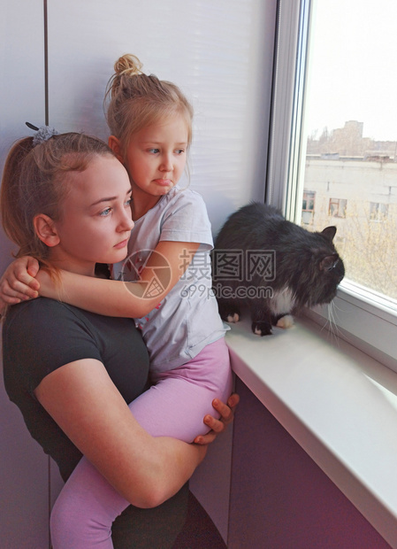 健康的坏伤心儿童和黑猫在隔离期间向窗外看望儿童想走出Corona检疫概念之外走悲伤姐妹和猫在隔绝女孩的期与可悲地从窗户外看猫在一图片