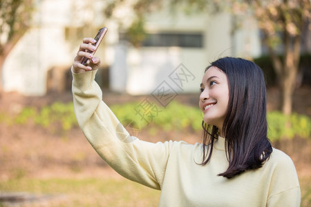 可爱的亚裔女正在使用手机取自拍和在家中花园笑摄影游客年轻的图片