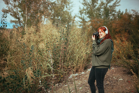 服用天芦苇年轻女子在森林里拍照用旧的模拟相机和耳拍摄图片