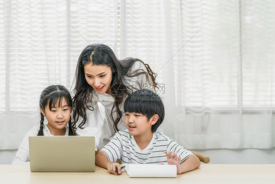 孩子们作业快乐的年轻亚洲单身母亲在家庭学校教育关系和家庭通信谈话概念中用电脑技术做家务工作或帮助女儿和子在家里教书或做务与庭有关图片