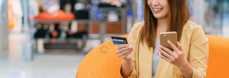 无卡支付卡片亚洲妇女使用信卡和移动电话在服装店商的百货在线购物技术钱包和网上付款概念信用卡模型等亚洲妇女用信卡和手机在互联网上买东西的情背景