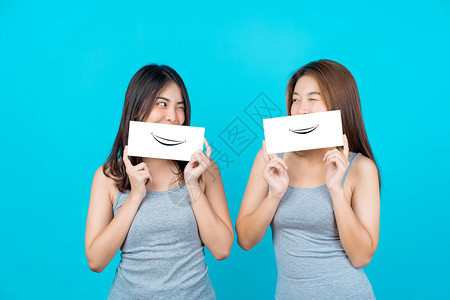 两个笑的亚洲青年妇女展示和关于孤立蓝色背景的海报在夏季室内工作穿防弹衣小册子和白广告纸等夏季室内工作木板的摆姿势图片