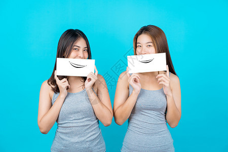 两个笑的亚洲青年妇女展示和关于孤立蓝色背景的海报在夏季室内工作穿防弹衣小册子和白广告纸等夏季室内工作女士为了季节图片