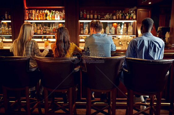 酒精闲暇坐着四位朋友在酒吧的柜台喝啤后视人群在吧放松晚上生活方式友谊动庆祝四位朋友在酒吧的柜台背视图片