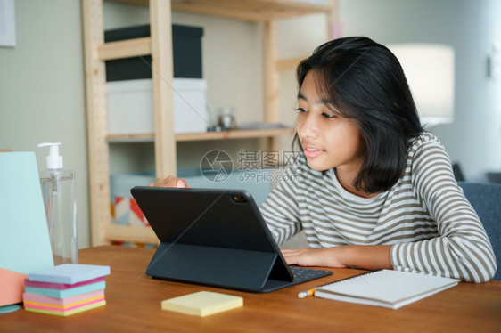 药片亚裔女孩坐在晚上的桌边透过互联网以平板数码方式在网上学习家庭在线概念女美丽的图片