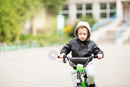 舵手穿着黑色皮夹克的可爱小城市男孩肖像风格孩子这男学会骑自行车孩子驾驶自行车孩子驾驶脚踏车脸城市的背景图片