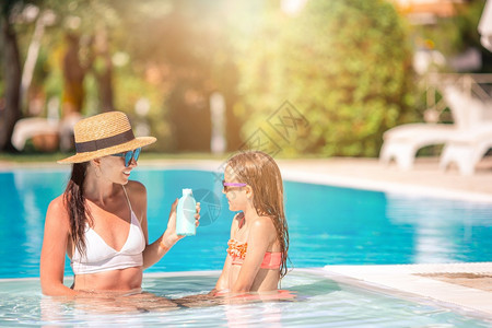 年轻妈妈在游泳池里给孩子涂防晒霜图片