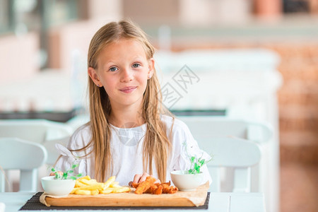 饥饿的孩子在户外咖啡厅吃早饭的可爱女孩在户外咖啡厅吃晚饭的可爱小女孩刀图片