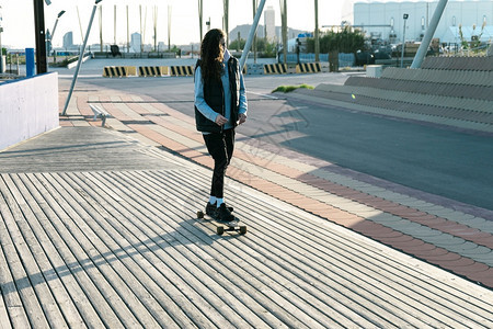 运输年轻女孩在阳光明媚的一天在城市公园的长板滑冰成人时髦图片