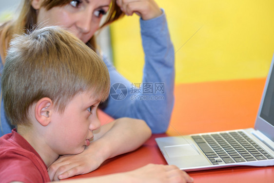 教育移民现代的一个小男孩在其母亲的监督下在笔记本电脑上工作或通信图片